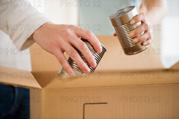 Close up of man's and woman's hands packing cans into box, studio shot. Photo : Jamie Grill