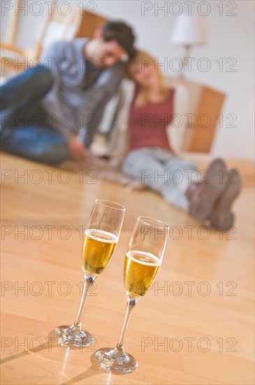 Close up of wine glasses on floor with couple behind. Photo : Daniel Grill