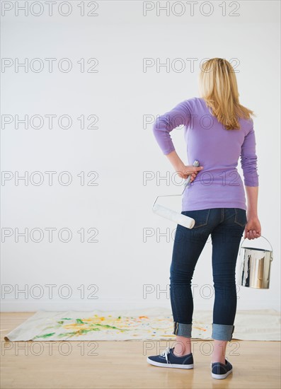 Rear view of woman holding paint can and paint roller. Photo : Daniel Grill