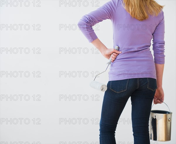 Rear view of woman holding paint can and paint roller. Photo : Daniel Grill