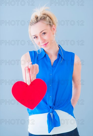 Portrait of smiling young woman holding red heart, studio shot. Photo : Daniel Grill