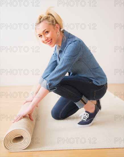 Young woman rolling up carpet, studio shot. Photo : Daniel Grill