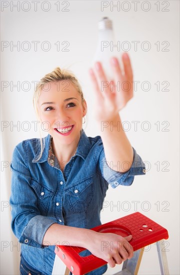 Young woman holding light bulb,  studio shot. Photo : Daniel Grill