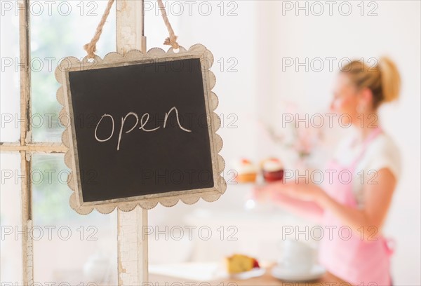 Close up of open sign with woman in background. Photo : Daniel Grill