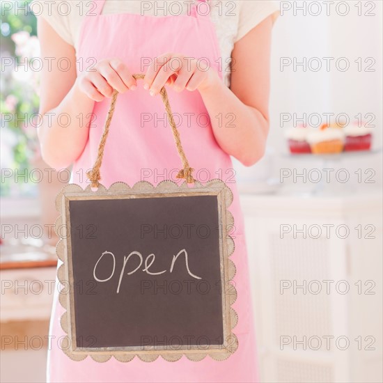 Close up of young woman in apron holding open sign. Photo : Daniel Grill