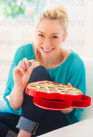 Smiling young woman eating chocolates. Photo : Daniel Grill