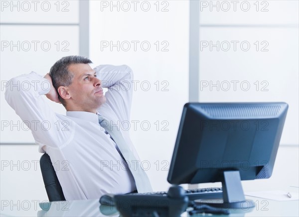 Portrait of businessman relaxing at desk. Photo : Daniel Grill