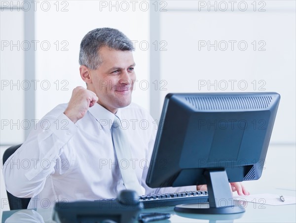 Portrait of happy businessman working at desk. Photo : Daniel Grill