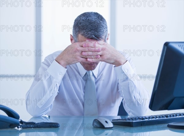 Portrait of depressed businessman sitting at desk. Photo : Daniel Grill