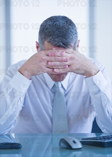 Portrait of depressed businessman sitting at desk. Photo : Daniel Grill