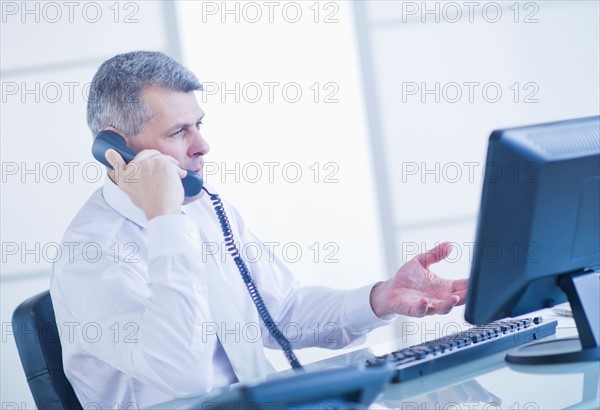Man sitting in office and talking on landline phone. Photo : Daniel Grill