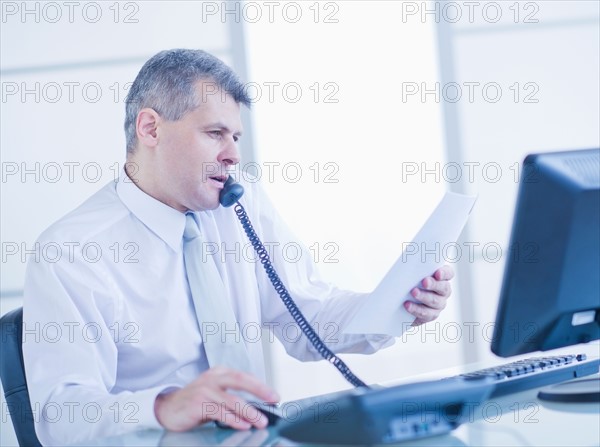 Man sitting in office and talking on landline phone. Photo : Daniel Grill