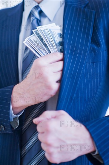 Businessman hiding banknotes in pocket. Photo : Daniel Grill