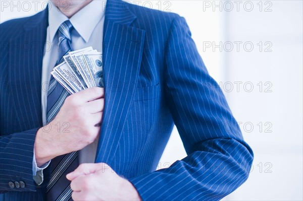 Businessman hiding banknotes in pocket. Photo : Daniel Grill