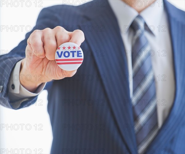 Man wearing suit holding vote pin. Photo : Daniel Grill