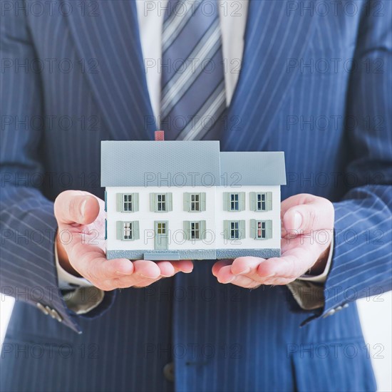 Man wearing suit holding small house model. Photo : Daniel Grill