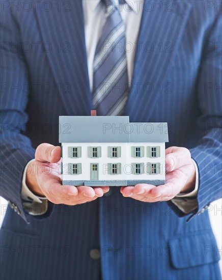 Man wearing suit holding small house model. Photo : Daniel Grill