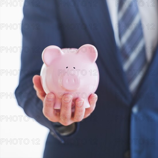 Man wearing suit holding piggybank. Photo : Daniel Grill