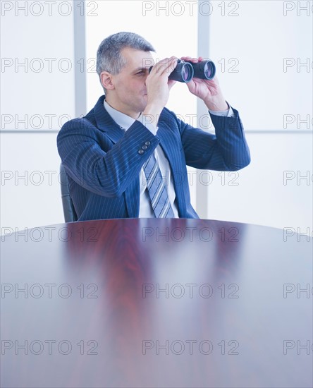 Portrait of businessman holding binoculars. Photo : Daniel Grill