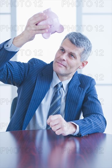 Businessman trying to get money from piggybank. Photo : Daniel Grill