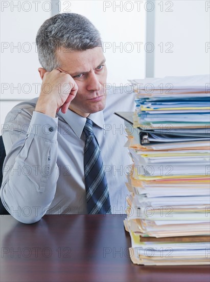 Businessman looking at large stack of documents. Photo : Daniel Grill