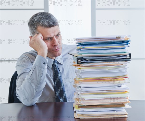 Businessman looking at large stack of documents. Photo : Daniel Grill