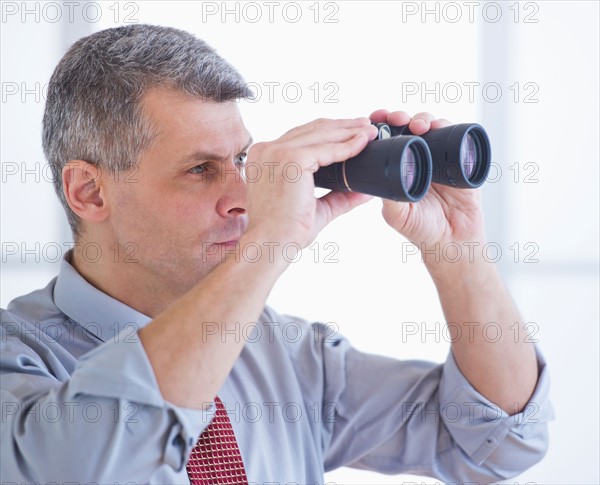 Portrait of businessman holding binoculars. Photo : Daniel Grill