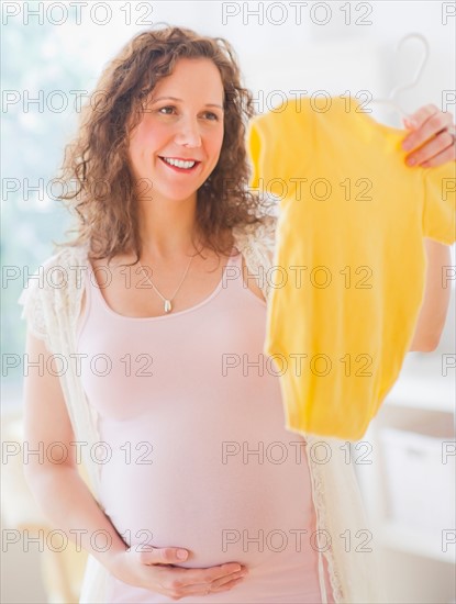 Portrait of pregnant woman holding baby clothes. Photo : Daniel Grill