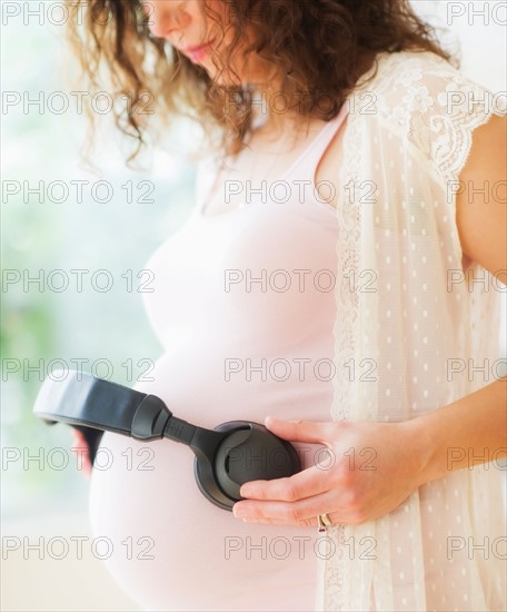 Portrait of pregnant woman holding headphones on her belly. Photo : Daniel Grill