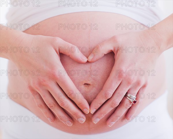 Pregnant woman with hands folded as heart on her belly. Photo : Daniel Grill