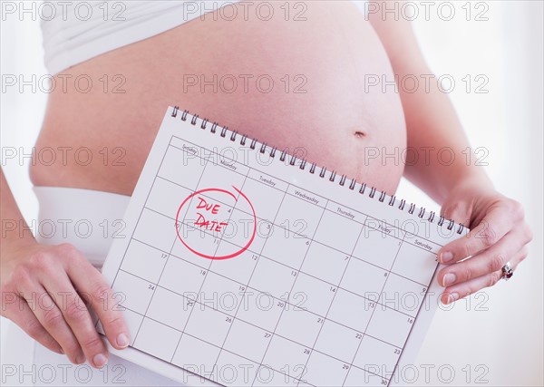 Pregnant woman holding calendar in front of her belly. Photo : Daniel Grill