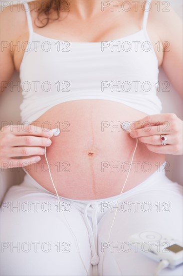 Pregnant woman holding earbuds on her belly. Photo : Daniel Grill