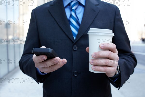 USA, New York, New York City. Businessman with smartphone and plastic cup. Photo : Winslow Productions
