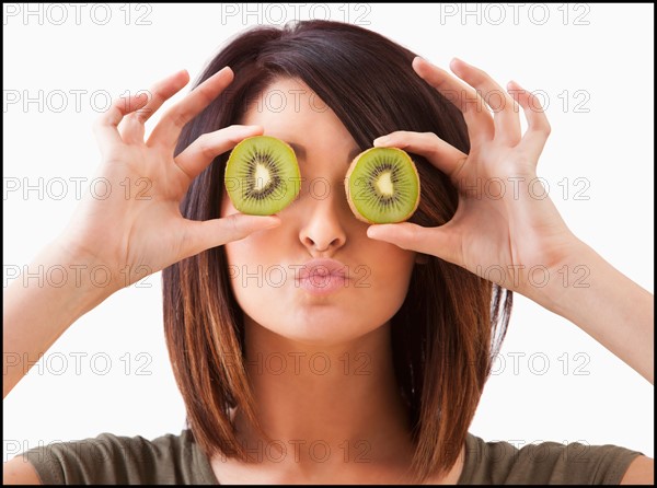 Young woman holding kiwi slices on eyes. Photo : Mike Kemp