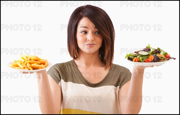 Young woman choosing between healthy and unhealthy food. Photo : Mike Kemp