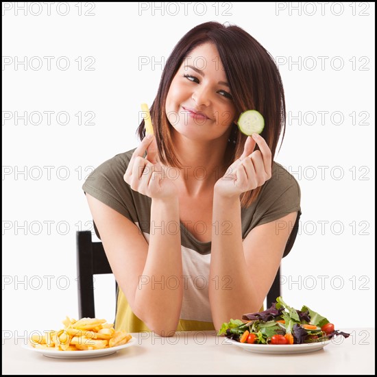 Young woman choosing between healthy and unhealthy food. Photo : Mike Kemp