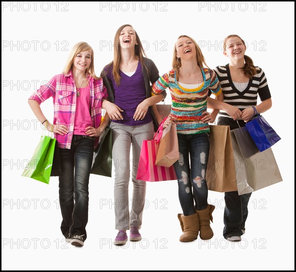 Studio shot of four happy girls (12-13) with shopping bags. Photo : Mike Kemp