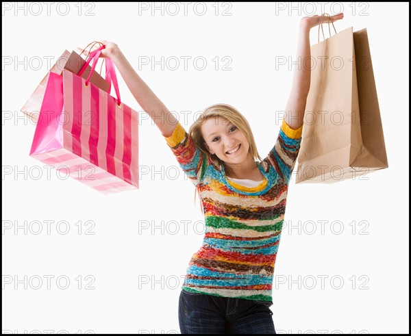 Studio shot of happy girl (12-13) with shopping bags. Photo : Mike Kemp