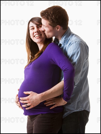 Man embracing pregnant woman, studio shot. Photo : Mike Kemp