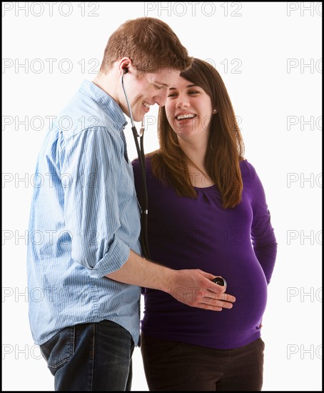 Man listening of heartbeating on belly of pregnant woman, studio shot. Photo : Mike Kemp