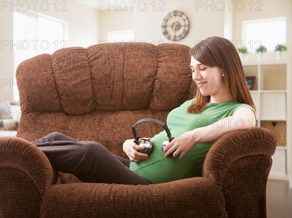 Portrait of pregnant woman sitting on sofa with headphones on her belly. Photo : Mike Kemp