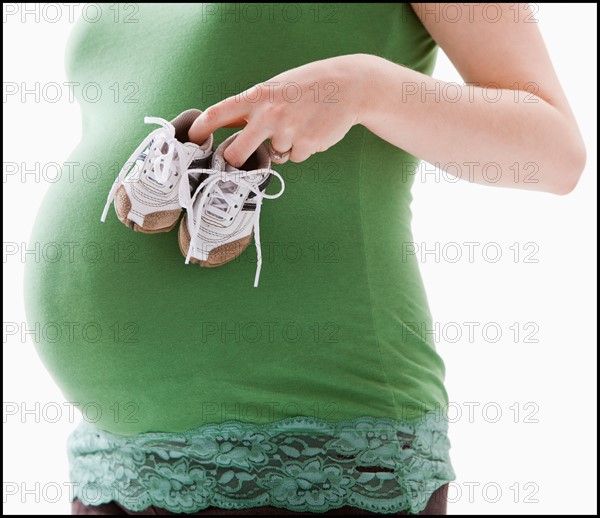 Studio Shot of mid section of pregnant woman holing baby booties. Photo : Mike Kemp
