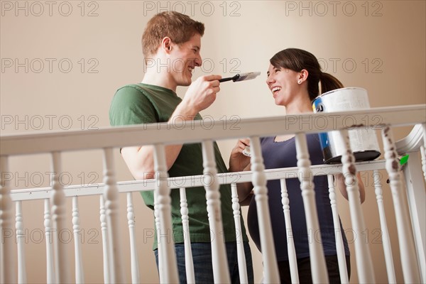 Young couple standing face to face holding paint brush. Photo : Mike Kemp