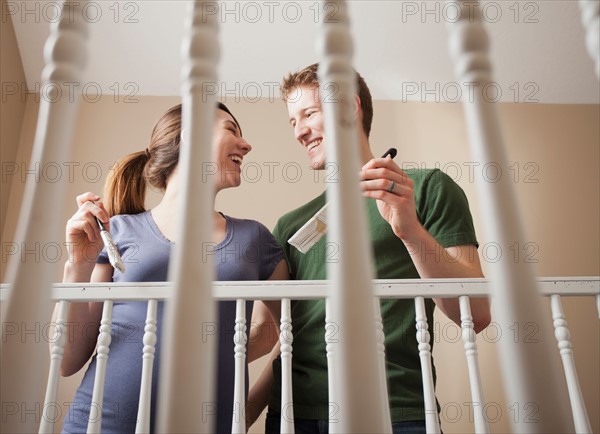 Low angle view of young couple standing face to face holding paint brush. Photo : Mike Kemp