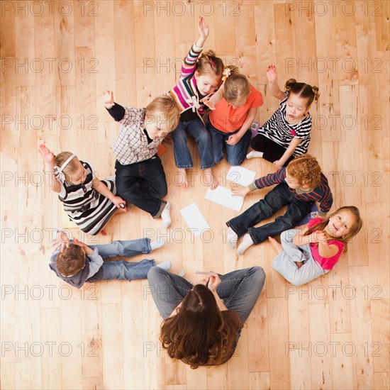 Children (2-3, 4-5) sitting on floor and raising hands, directly above. Photo : Mike Kemp