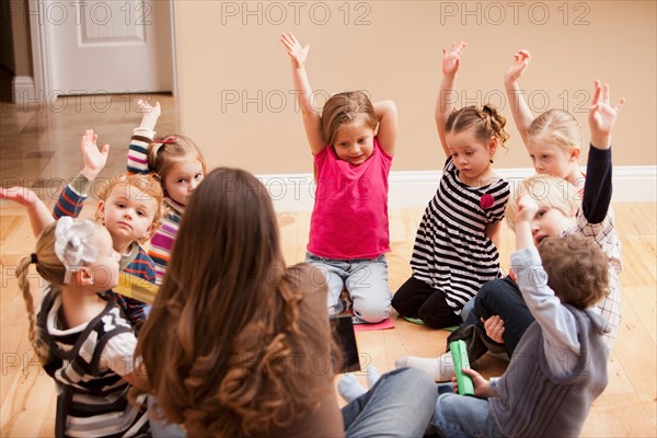 Children (2-3, 4-5) sitting on floor and raising hands. Photo : Mike Kemp