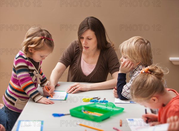 Mid adult woman teaching children (2-3, 4-5) drawing in kindergarten. Photo : Mike Kemp