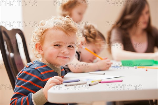 Boy (4-5)  looking at camera during art lesson in kindergarten. Photo : Mike Kemp