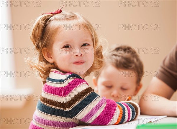 Girl (2-3) looking at camera during art lesson in kindergarten. Photo : Mike Kemp