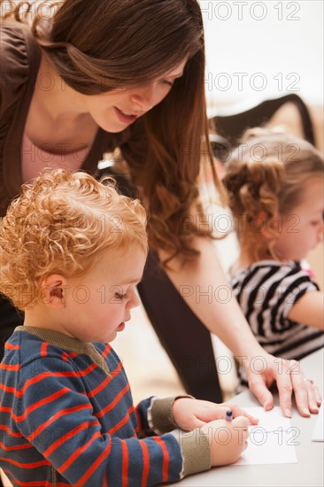 Mid adult woman teaching boy (4-5) drawing in kindergarten. Photo : Mike Kemp